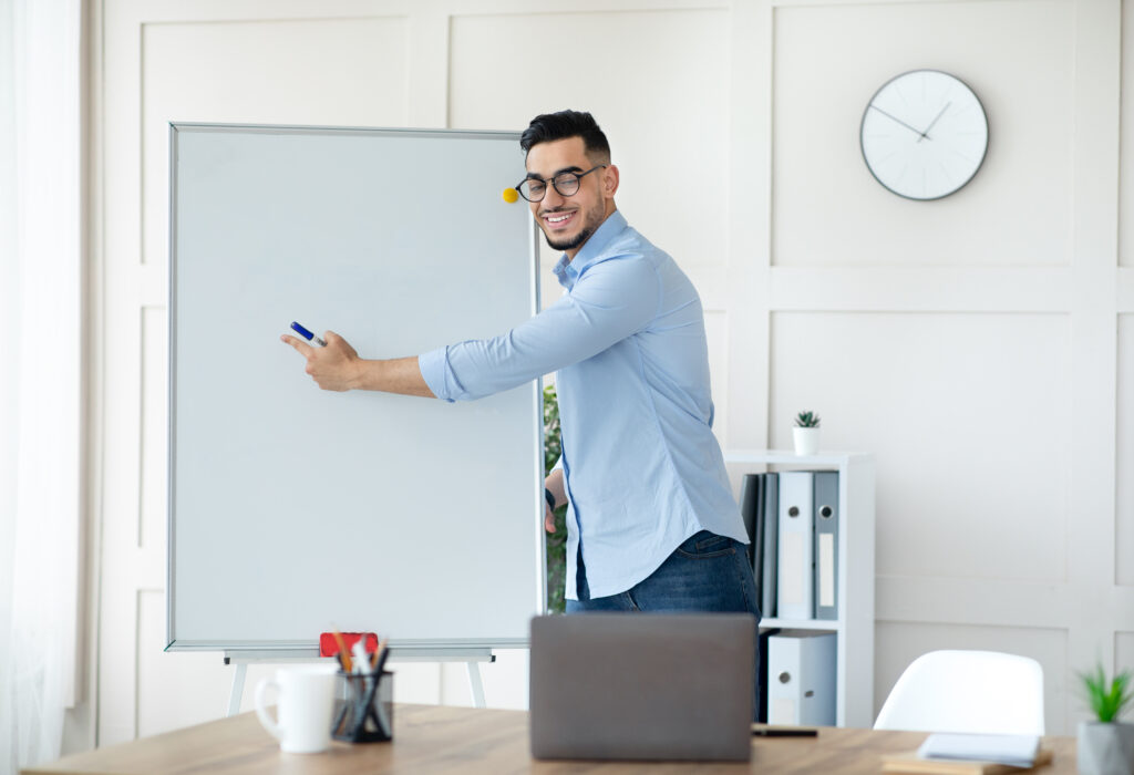 Confident Arab male tutor pointing at empty blackboard with mockup for design, giving web lesson on