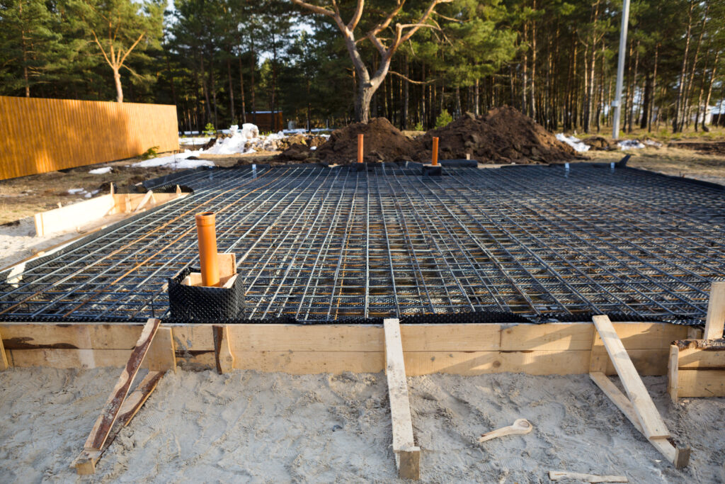 Iron fittings on a wooden formwork with laid pipes are the basis for pouring the foundation