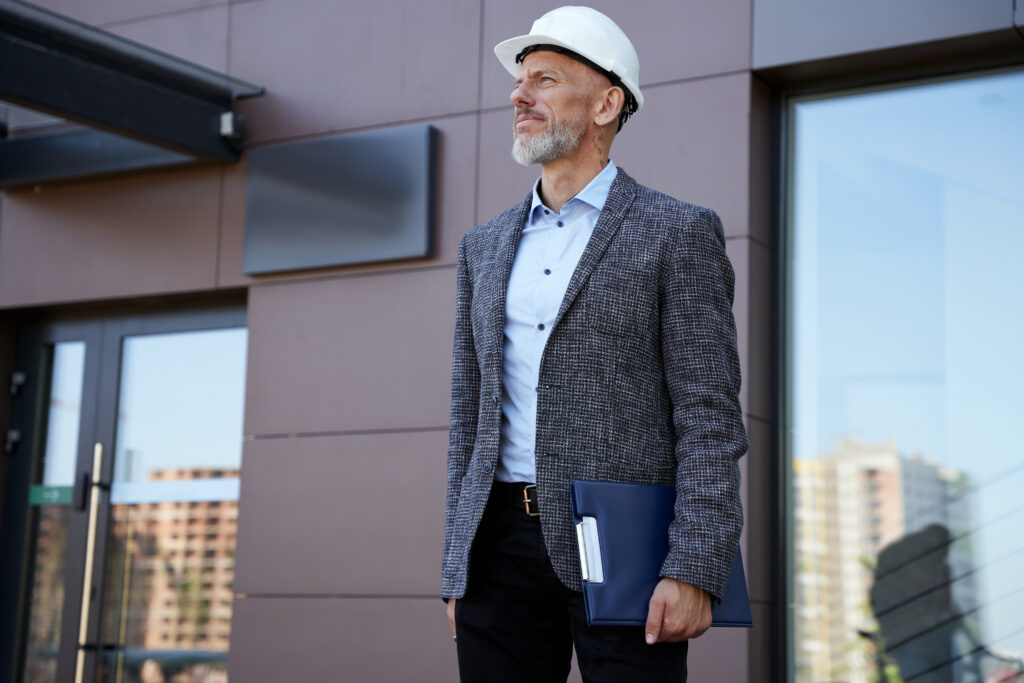 Monitoring the progress. Focused middle aged architect, engineer manager wearing helmet looking