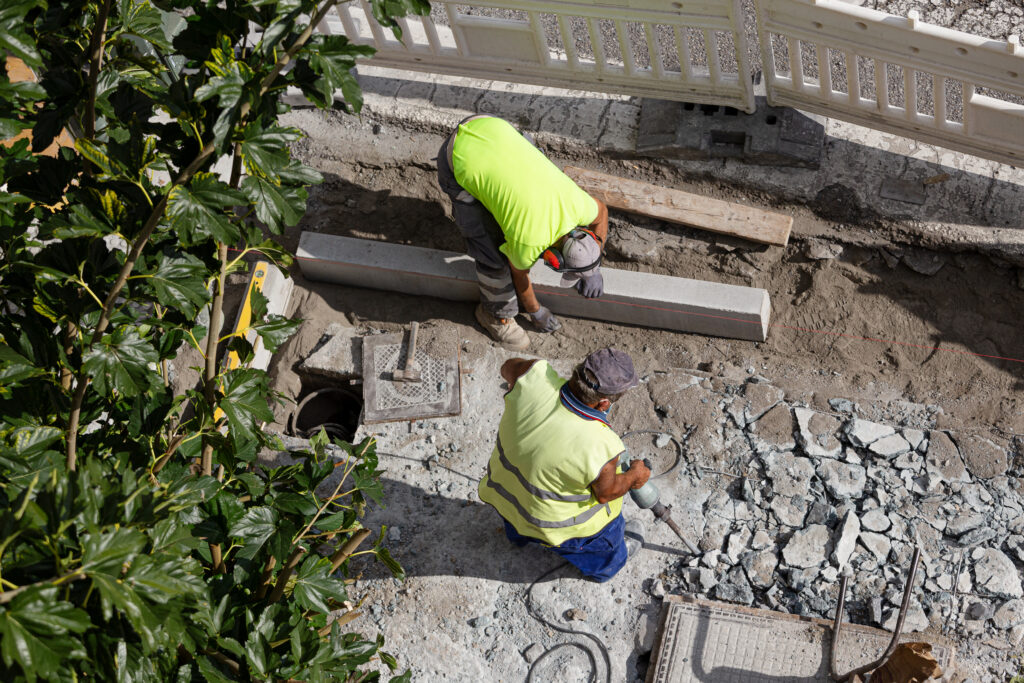 Construction worker with jackhammer drilling concrete on sidewalk