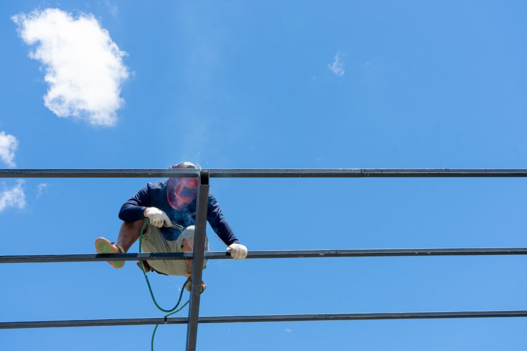 Welder welds the steel structure on the structure of roof with clear sky background