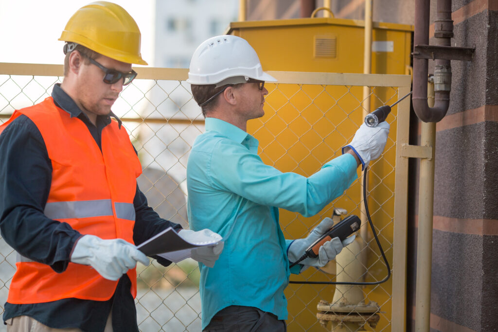 young men are standing near the gas pipe at the house with an analyzer and documents