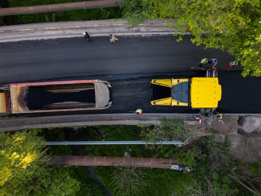 Aerial view of the construction of a new road as asphalt pavers, rollers, machinery, and workers